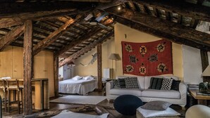 Een rustieke kamer met zichtbare houten balken, een bed, een bank en een eethoek.