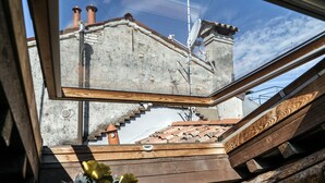 Uitzicht door een dakvenster op de buitenkant van een gebouw, met een stenen muur, een pannendak en een schoorsteen.