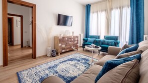 Ein Wohnzimmer mit einer Couch, einem Couchtisch, einem Fernseher und einem blau-weißen Teppich mit Muster.
