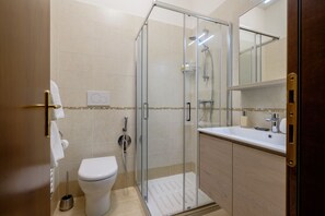 A modern bathroom with a glass-enclosed shower, a toilet, and a sink with a mirror above it.