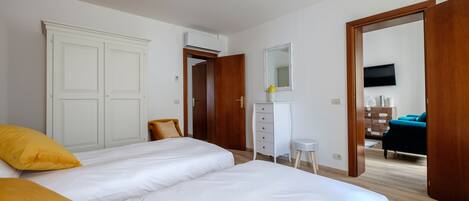 Une chambre avec deux lits, une commode, un miroir et une porte ouverte donnant sur une autre pièce.
