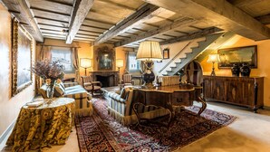 Ein traditionell eingerichteter Raum mit freiliegenden Holzbalken, Kamin, Sofa, Tisch und Treppe.