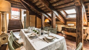 Ein Essbereich mit hoher Holzbalkendecke, einem für vier Personen gedeckten Tisch und einer Treppe, die zu einer oberen Ebene führt.