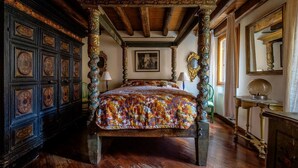 Un lit à baldaquin avec une couvre-lit aux couleurs vives, une armoire en bois foncé ornée de panneaux décoratifs et un grand miroir accroché au mur.