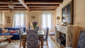 Un salon avec un canapé bleu, des fauteuils à motifs, une cheminée en marbre et un lustre.