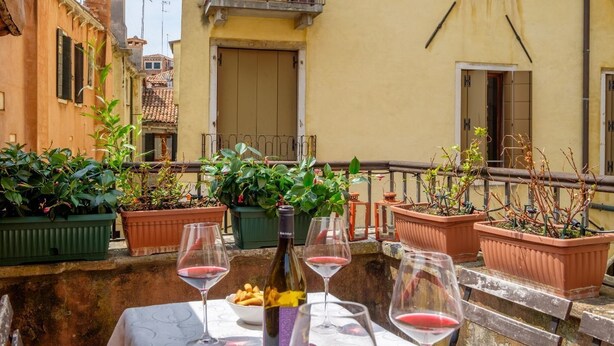 Une terrasse agrémentée de plantes en pot, une table avec des verres à vin et une bouteille de vin.