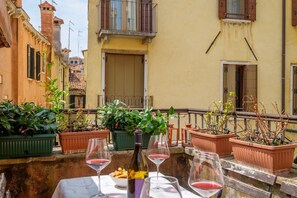 A terrace with potted plants, a table with wine glasses, and a bottle of wine.