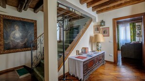 Un escalier avec une rampe en verre, un plafond en bois, un tableau encadré, une table avec des livres et une lampe.
