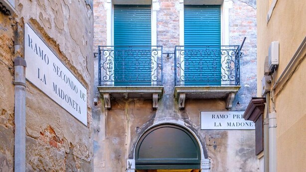 A narrow alleyway with a building entrance, two signs reading "RAMO SEGUNDO DE LA MADONETA" and "RAMO PRI LA MADONETA," and a staircase leading to a second floor with a balcony. - Ca' del Ramo D'oro (Venice)