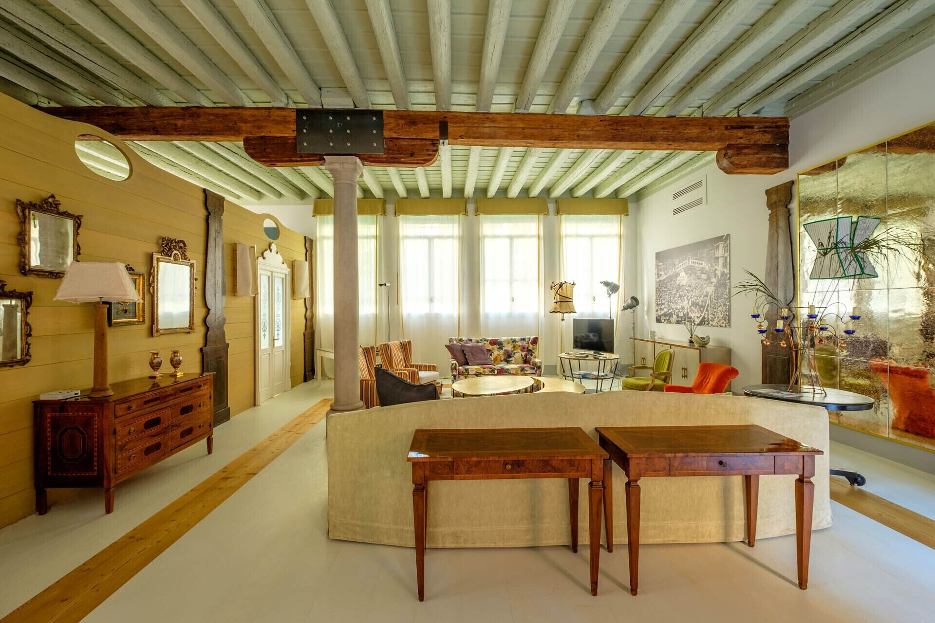 Un salon spacieux avec un plafond haut, des poutres apparentes, un espace salon central comprenant un canapé et des fauteuils, une table basse et un téléviseur.