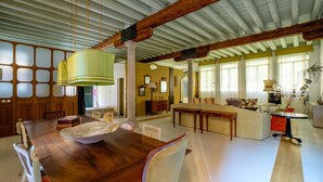 A spacious living room with a wooden dining table, a large green pendant light, and a high ceiling with exposed beams. - Ca' del Ramo D'oro (Venice)