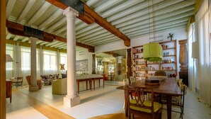 A spacious living area with a high ceiling, wooden beams, a large bookshelf, and a dining area with a wooden table and chairs. - Ca' del Ramo D'oro (Venice)