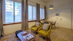 A hotel room with a large window, two yellow armchairs, a wooden coffee table, a small table with chairs, and a door. - Guarana (Venice)