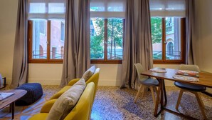 A room with a sofa, a dining table with chairs, and large windows with curtains. - Guarana (Venice)