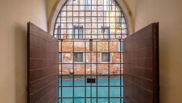 A narrow corridor with a metal gate leading to a courtyard with a brick wall and a window. - Palazzo Ca' Moro apartments (Venice)