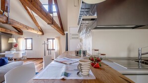 A modern kitchen with wooden beams, a dining area with a wooden table, and a kitchen island with a newspaper and mug. - Palazzo Ca' Moro apartments (Venice)