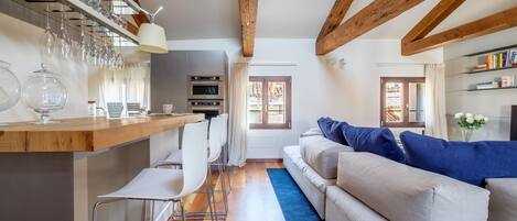 A modern kitchen with a wooden beam ceiling, a bar area with stools, and a sofa with blue cushions.