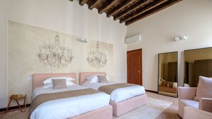 A hotel room with two beds, a chandelier, an air conditioning unit, and a large mirror. - Palazzo Ca' Moro apartments (Venice)