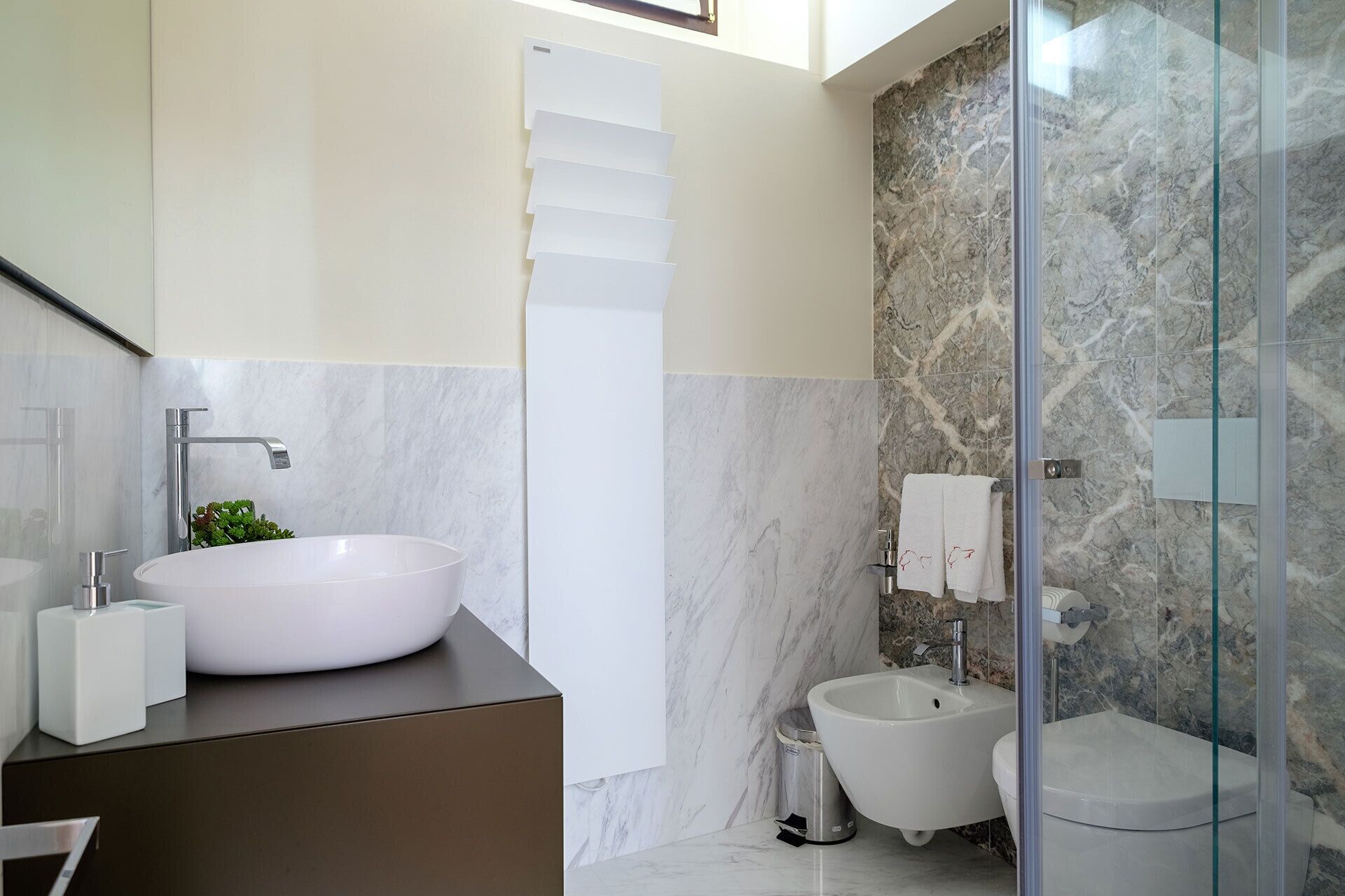 Un bany modern amb un gran lavabo blanc, un vàter i una cabina de dutxa de vidre.