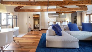 A spacious living area with a high ceiling and exposed wooden beams, a modern kitchen with stainless steel appliances, and a dining area with white furniture. - Palazzo Ca' Moro apartments (Venice)