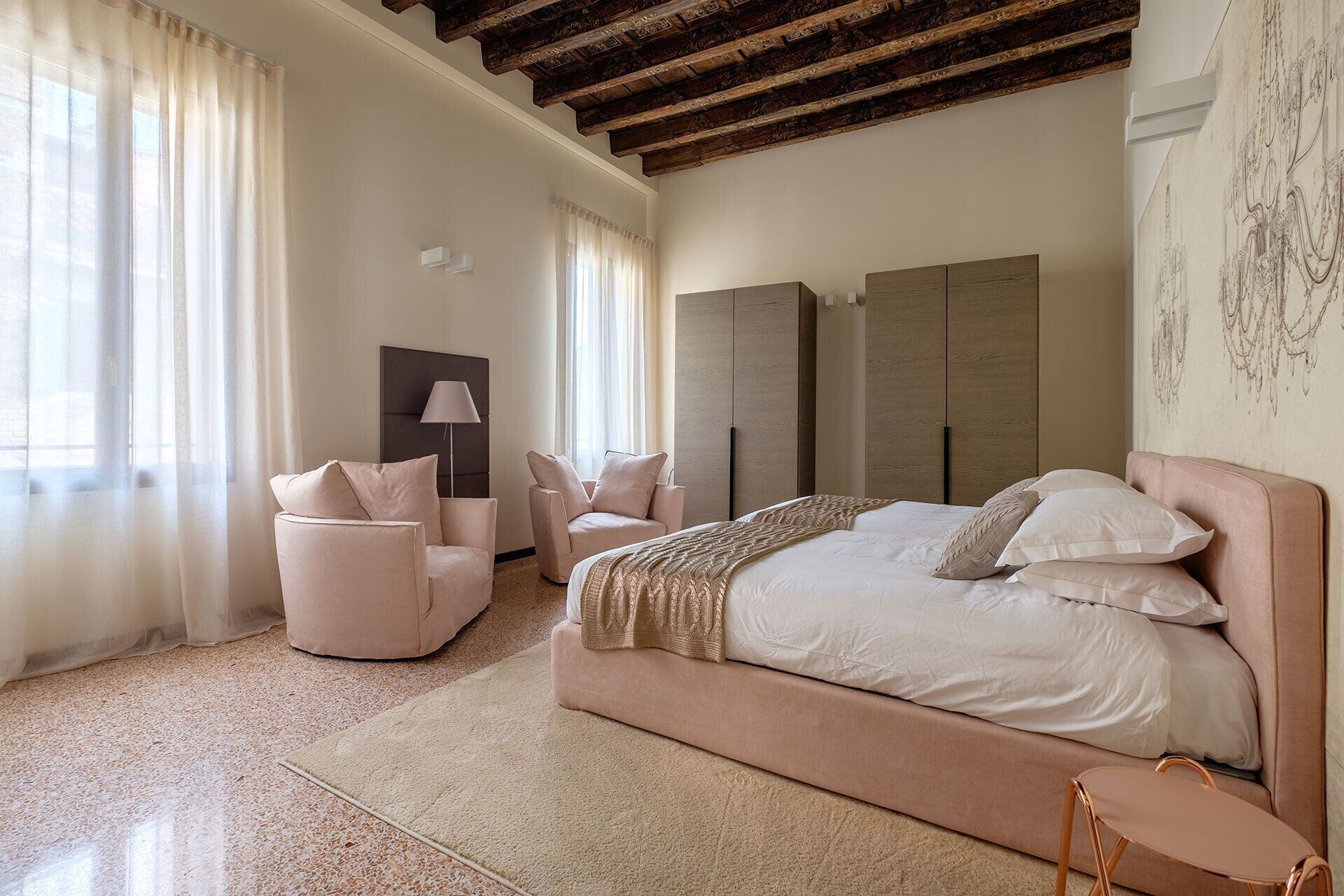 A bedroom with a large bed, two chairs, a floor lamp, and a wardrobe.