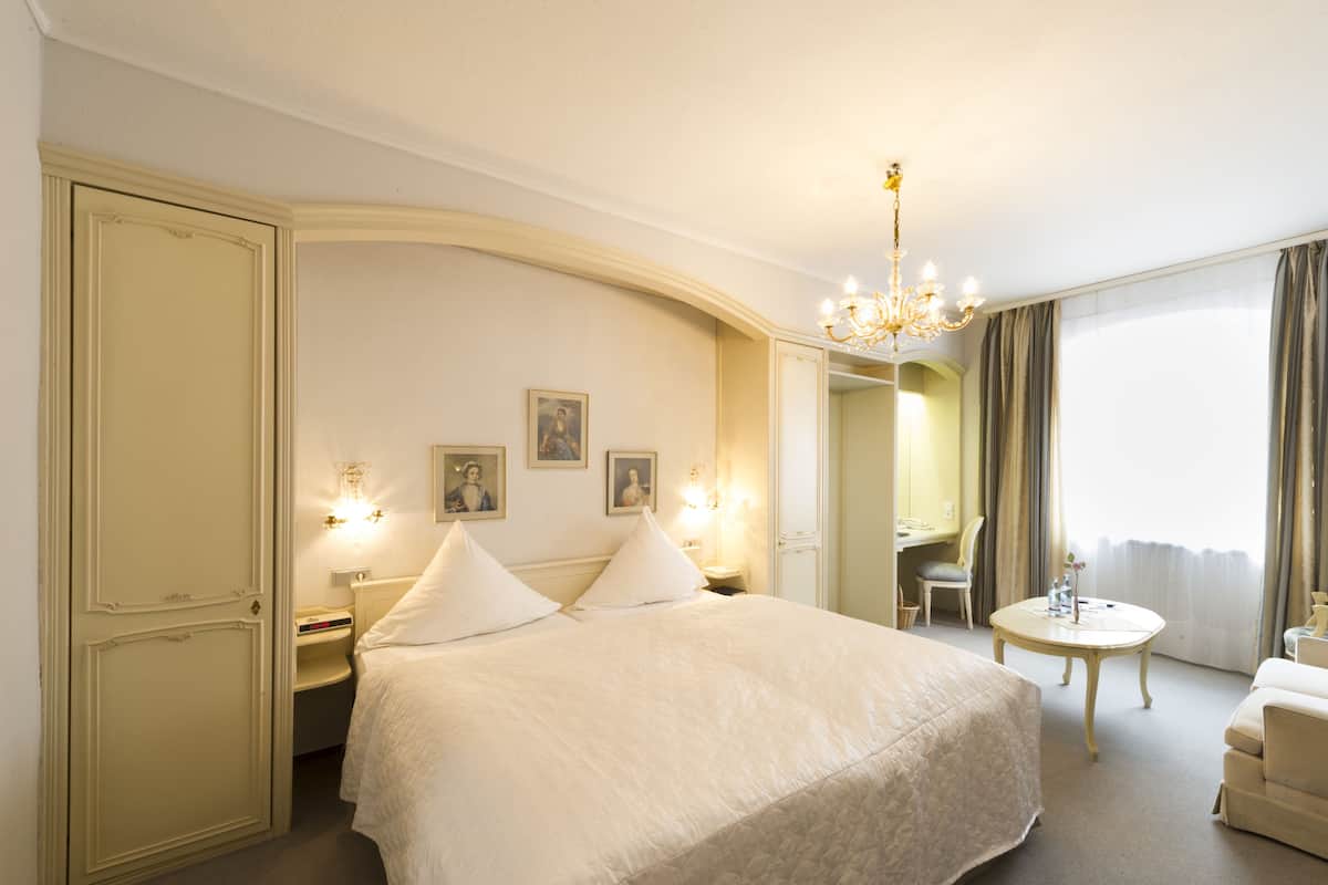 A hotel room with a large bed, a desk, a chair, and a small table.