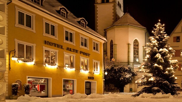 A hotel with a clock tower, snow-covered surroundings, and a decorated Christmas tree. - Alte Post (Wangen im Allgäu)