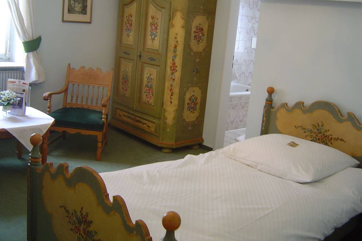 A bedroom with a wooden bed, a green upholstered chair, and a vintage wooden wardrobe.
