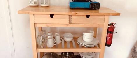 A wooden kitchen cart with shelves holding white mugs, plates, and cookware.