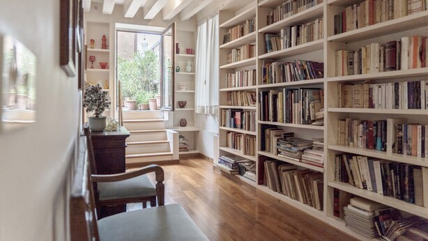 Una biblioteca con estanterías de madera, una mesa de madera y una ventana con vistas al verdor.