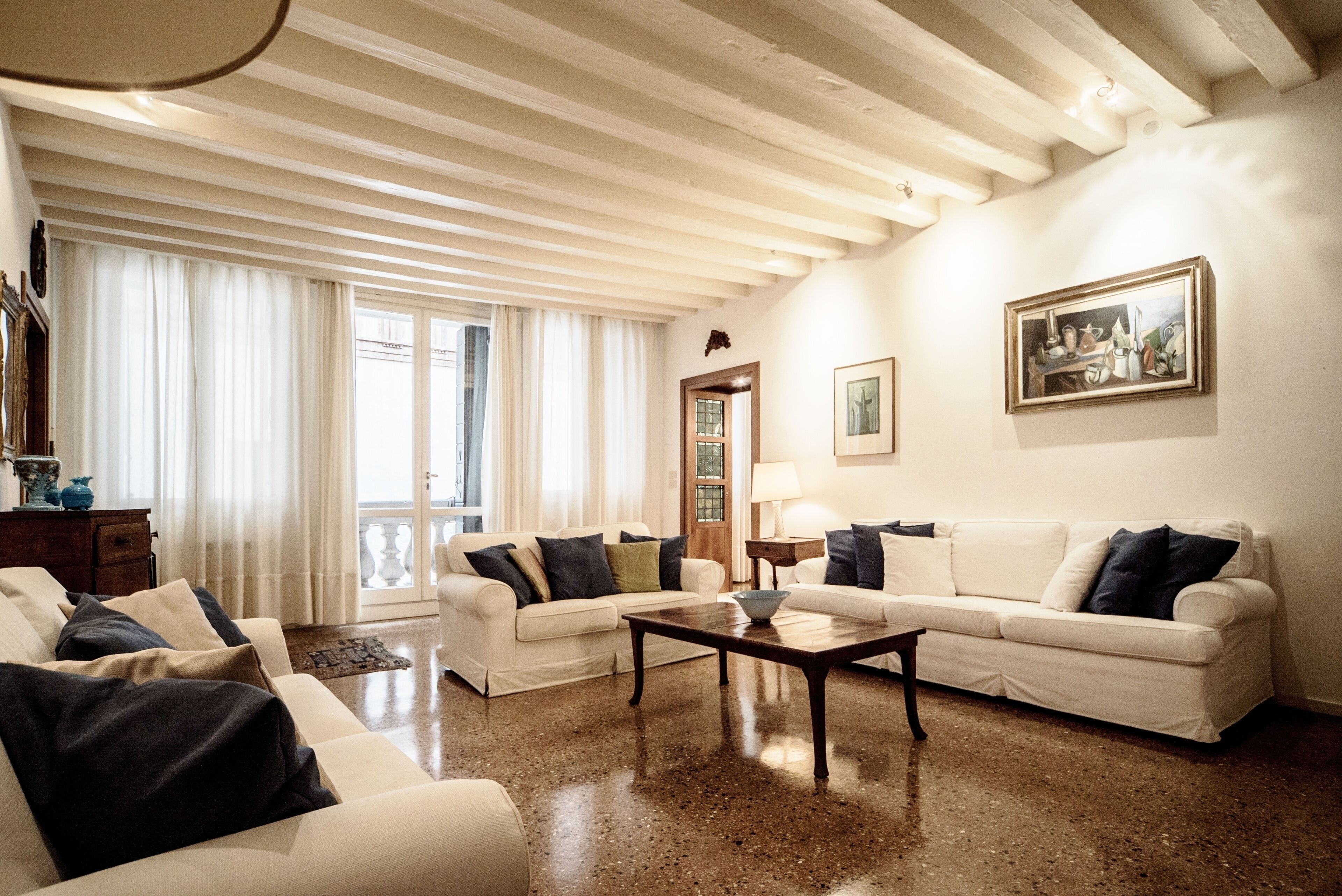 Un salon spacieux avec un plafond haut, des canapés blancs, une table basse et un tableau accroché au mur.