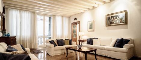Un salon spacieux avec un plafond haut, des canapés blancs, une table basse et un tableau accroché au mur.
