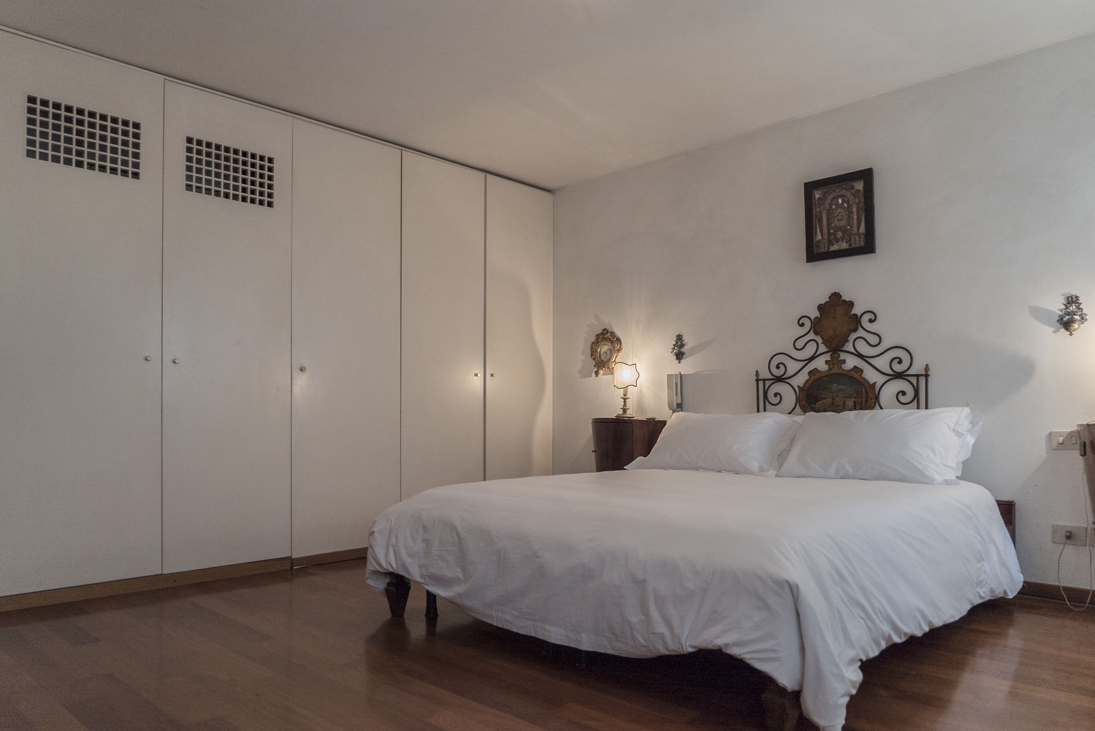 Un dormitorio con una cama grande, un armario y una mesita de noche con lámpara.