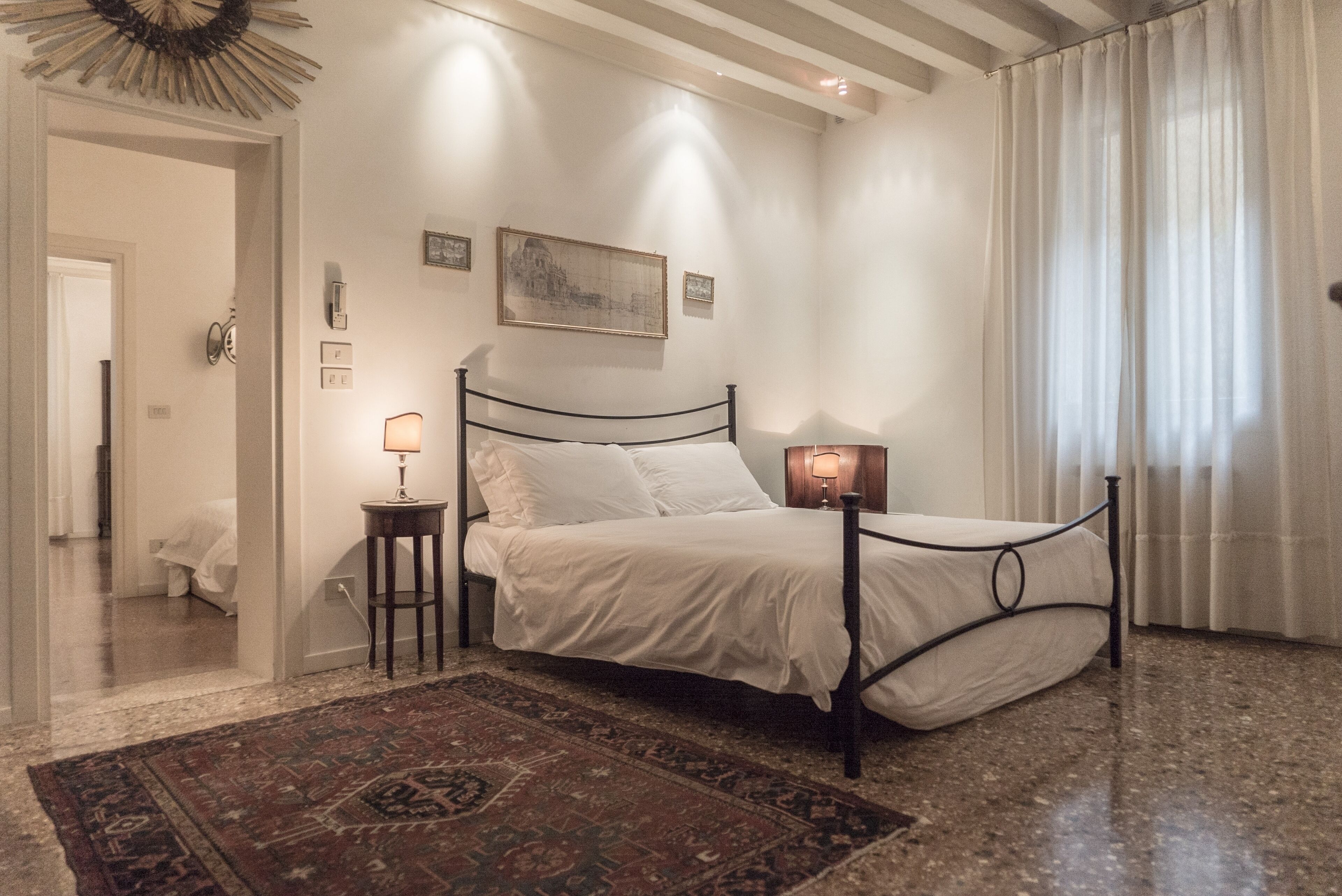 A bedroom with a bed, bedside lamps, a rug, and a painting on the wall.