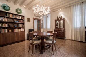 Uma área de refeições com uma mesa redonda de madeira, quatro cadeiras, um lustre, uma estante de livros e um espelho.