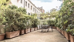 Un patio con una mesa y sillas, rodeado de plantas en macetas y un edificio al fondo.