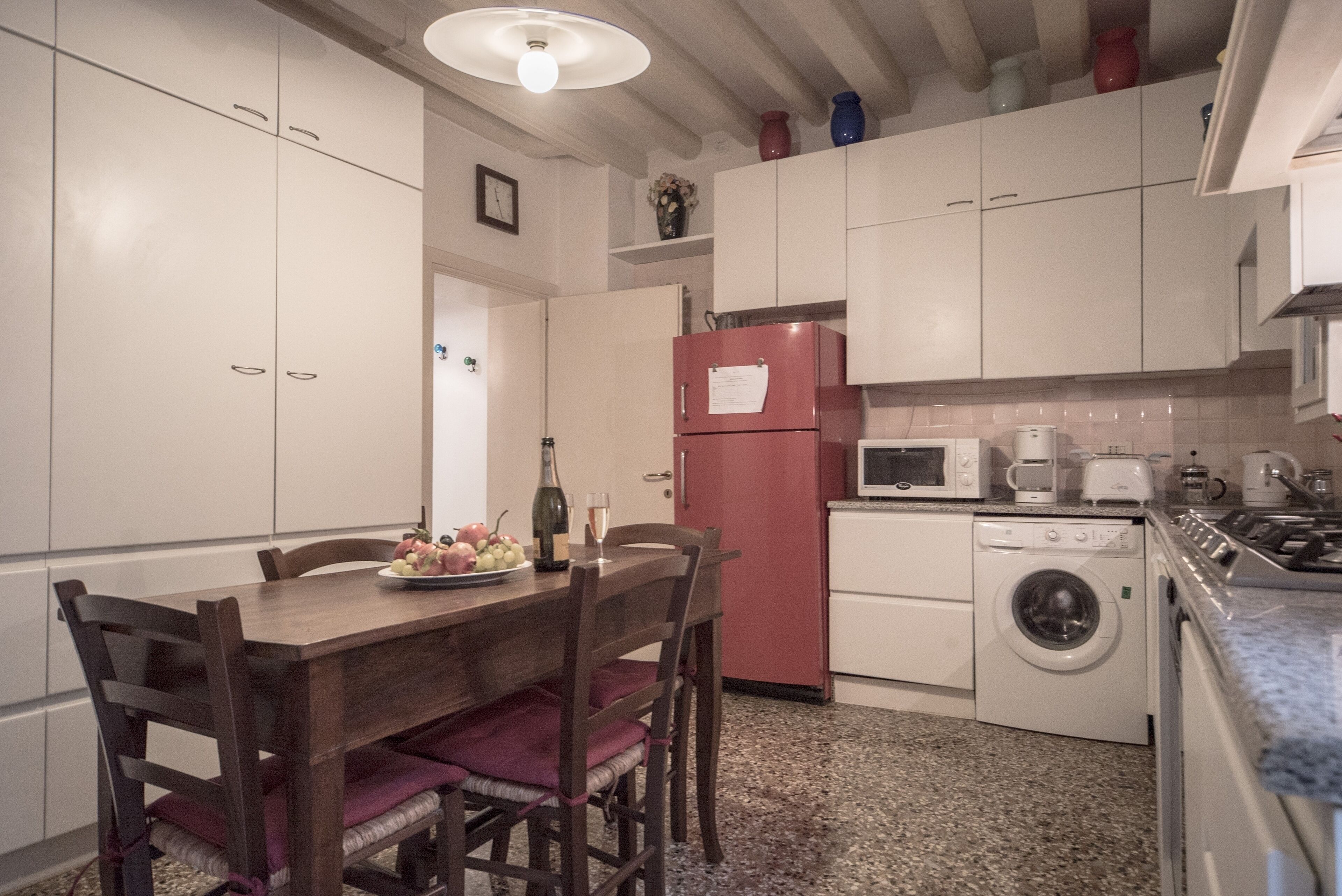 Una cuina compacta amb armaris blancs, un frigorífic vermell, una rentadora i una taula de menjador amb cadires.