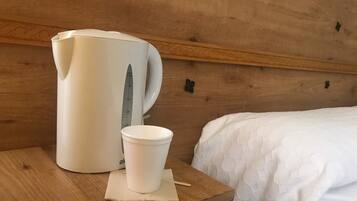 Cabecera de madera con colcha blanca y una taza blanca sobre una mesita de noche de madera.