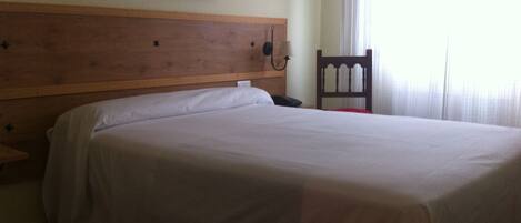 A single bed with a wooden headboard, a bedside table, a chair, and a wall-mounted telephone.