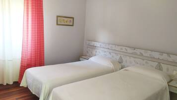 Een hotelkamer met twee eenpersoonsbedden, een rood gordijn, een ingelijst kunstwerk aan de muur en een bedkap met een patroon.
