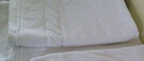 Neatly folded white towels stacked on a bed.