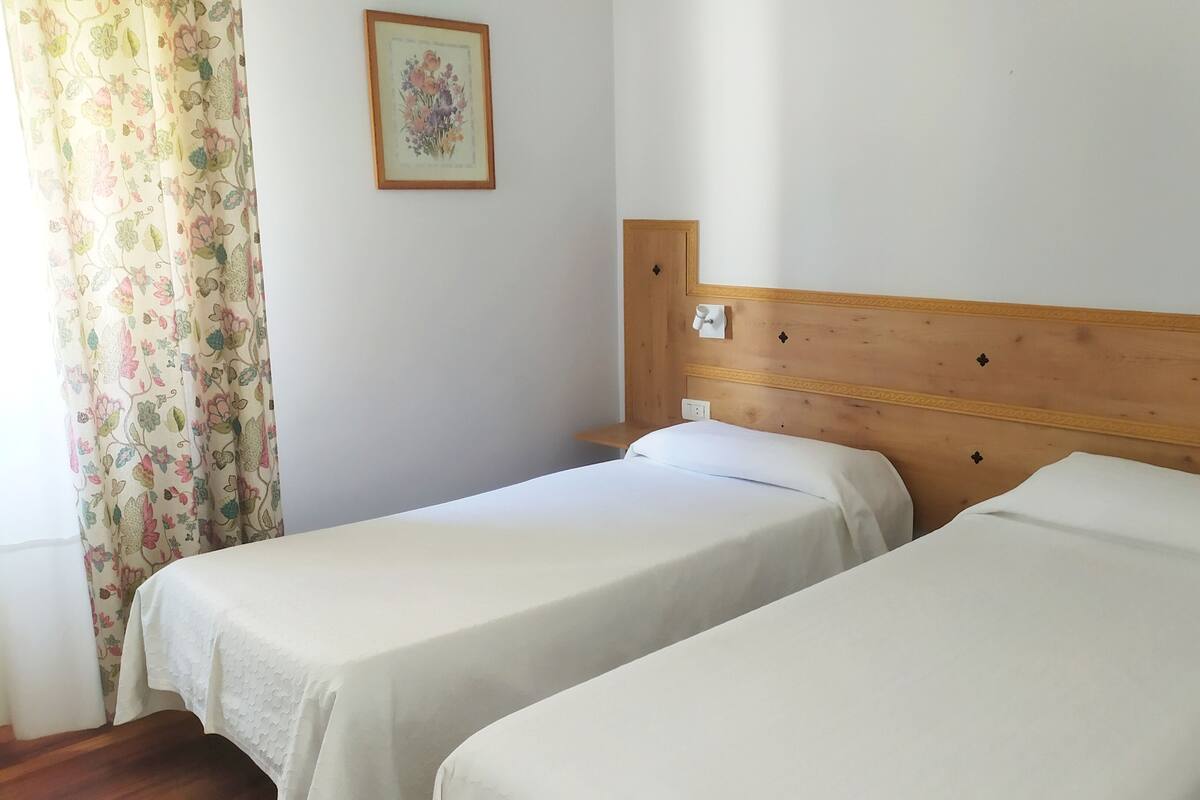 A room with two single beds, a wooden headboard, a floral curtain, and a framed picture on the wall.