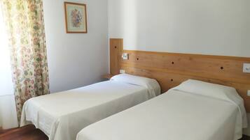 A room with two single beds, a wooden headboard, a floral curtain, and a framed picture on the wall.