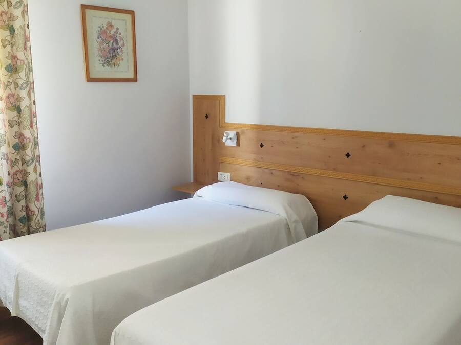 A room with two single beds, a wooden headboard, a floral curtain, and a framed picture on the wall.