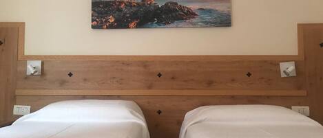 Habitación de hotel con dos camas individuales, un cabecero de madera y un cuadro de un faro en la pared.