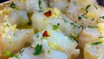 A close-up of a dish with diced fish, garnished with herbs and red pepper flakes.