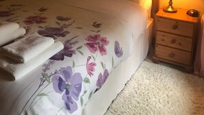 A neatly made bed with floral bedding, a bedside lamp, and a small wooden nightstand with a clock. - Hosefield Bed and Breakfast (Ellon)
