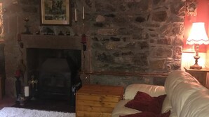 A cozy living room with a stone wall, a fireplace, a white leather sofa, and a wooden chest. - Hosefield Bed and Breakfast (Ellon)