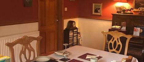 A dining room with a table set for two, featuring a box of Kellogg's Corn Flakes cereal, a clock, and a lamp.