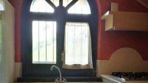A kitchen with a double sink, a window with a curtain, and a stove. - Villa Agreste (Cupello)